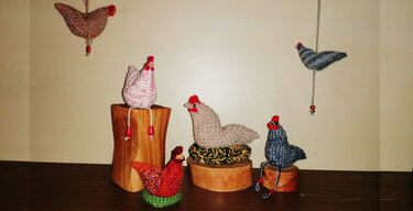 Gehäkelte Amigurumi‑Hühner in Pastell- und Erdtönen auf Holzpodesten und hängend
