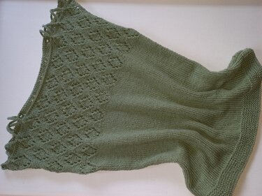 Salbeigrünes gestricktes Damen-Top mit Ajourmuster oben und glatt rechts gestricktem Unterteil auf hellem Hintergrund.