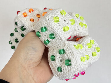 Hand holding a white crocheted ball of joined motifs decorated with translucent green, yellow, orange and pink beads