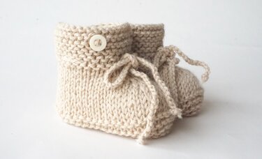 paar handgestrickter cremefarbener Babyschuhe mit Knopf und Schnürung