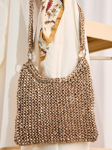 Gehäkelte goldene Umhängetasche mit kettenähnlichem Riemen an einem hellen Kleidungsstück hängend