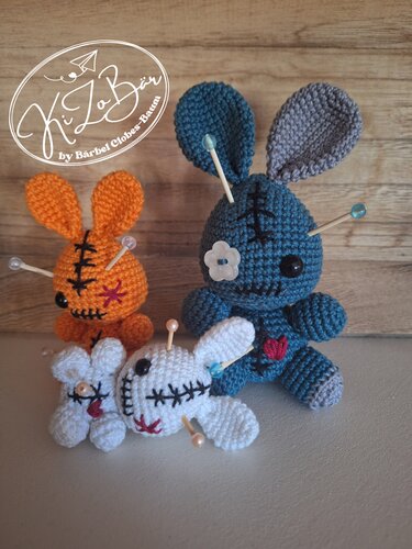 Drei gehäkelte Amigurumi-Hasen (orange, blau, weiß) mit aufgestickten Nähten und Stecknadeln