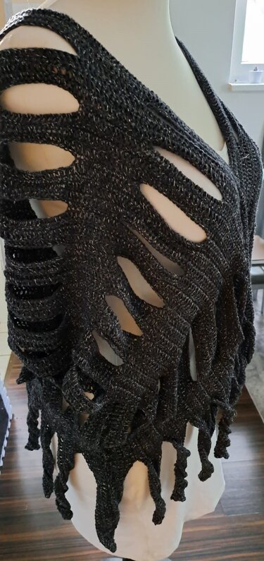 Dunkelgrauer gehäkelter Poncho mit großen unregelmäßigen Öffnungen und silbernen Glitzerfäden an einer Schneiderpuppe