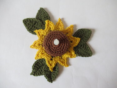 Gehäkelte Sonnenblume mit braunem Kern und drei grünen Blättern