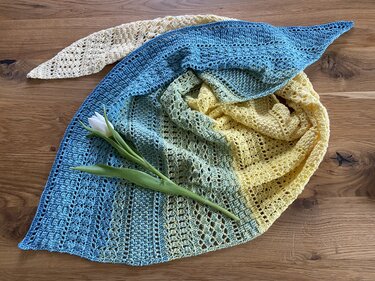 Handgehäkeltes Dreieckstuch mit Farbverlauf von Blau über Grün zu Gelb auf Holztisch mit weißer Tulpe