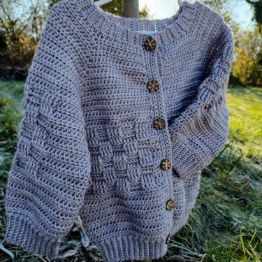 Gehäkelte hellgraue Babyjacke mit Holzknöpfen an Kleiderbügel