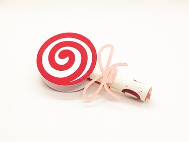 Paper craft lollipop with red spiral top and separate pink bow on white