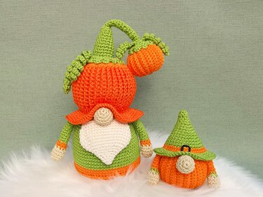Zwei gehäkelte Amigurumi-Kürbis-Wichtel in Orange und Grün, einer mit Mini-Kürbis am Stiel