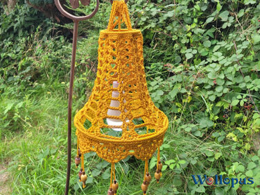 Senfgelber gehäkelter Lampion mit Holzperlen vor grünem Gebüsch