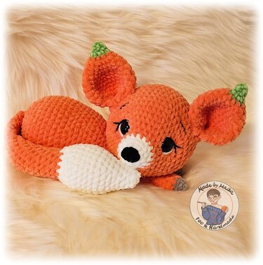 Gehäkelter orangefarbener Amigurumi-Fuchs liegend auf hellem Fell