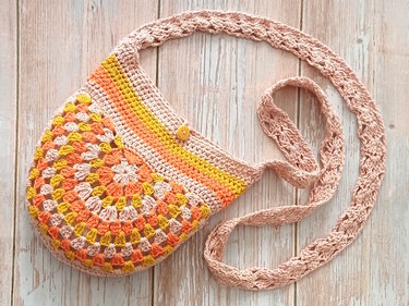 Gehäkelte Umhängetasche mit rundem Granny‑Muster in Gelb, Orange und Pfirsich sowie langem Träger und Knopf