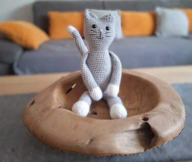 Gehäkelte graue Katze mit weißen Pfoten in einer Holzschale