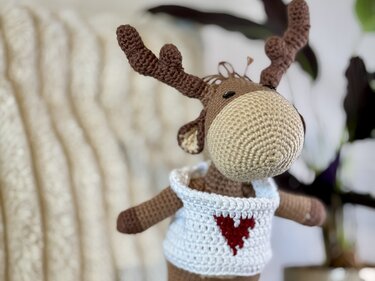 Gehäkeltes Amigurumi‑Rentier in Braun und Beige mit weißem Pullover und rotem Herz