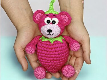 Hand hält gehäkelten pinken Amigurumi-Teddy mit grüner Blattkrone