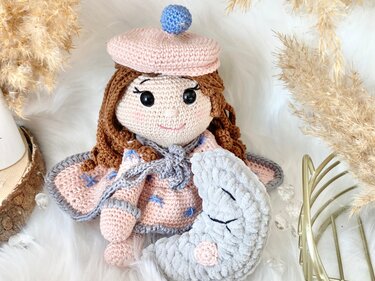 Gehäkelte Amigurumi-Puppe in Rosa mit Flügeln hält ein graues Mondkissen