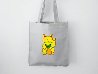 Graue Stofftasche mit gelber Winkekatze in der Mitte