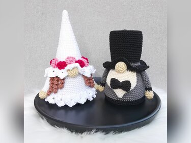 Gehäkelte Braut- und Bräutigam-Wichtel nebeneinander, Braut mit Blumenkranz, Bräutigam mit Zylinder und Fliege