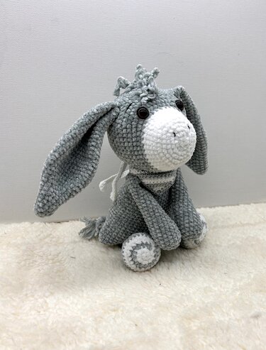 Gehäkelter grauer und weißer Esel-Amigurumi sitzend mit gestreiftem Halstuch