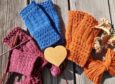 Fingerlose Damen-Handstulpen mit Rippenbündchen und strukturiertem Muster neben Stricknadeln und Garn