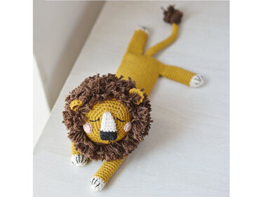 Gehäkelter Löwe-Amigurumi in Senfgelb liegend mit brauner Mähne