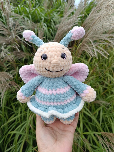 Gehäkelter Amigurumi-Schmetterling aus Plüschgarn mit Fühlern, Flügeln und gestreiftem Kleid in Pastellfarben
