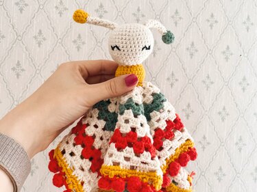 Detailansicht eines gehäkelten Schmusetuchs im Käfer-Design mit buntem Granny-Square-Muster, von einer Hand präsentiert