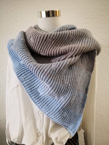 Gestricktes dreieckiges Tuch in Blau‑Grau mit Rippenstruktur und kleinen Quadraten, auf Schaufensterpuppe drapiert