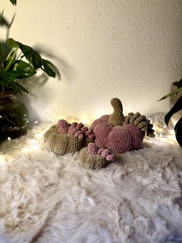 Drei gehäkelte Kürbisse in Rosé und Beige auf weißem Fell mit Lichterkette