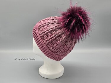 Gehäkelte rosafarbene Mütze mit breitem Rippenbund und großem Bommel auf weißer Büste