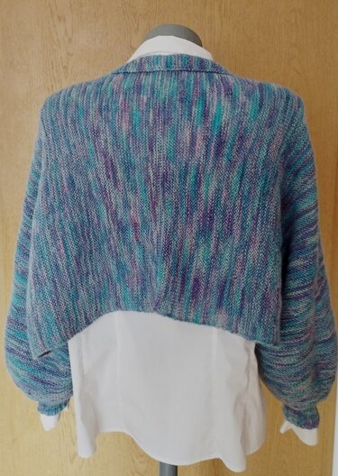 Rückansicht eines kurz geschnittenen gestrickten Seelenwärmers in Blau- und Lilatönen über weißem Hemd