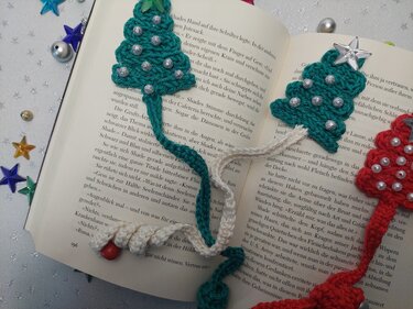 Gehäkelte Tannenbaum-Lesezeichen in Grün und Rot mit Perlen, Sternen und gedrehter Kordel auf offenem Buch