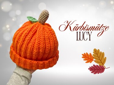 Orange gehäkelte Kürbismütze in Kürbisform mit braunem Stiel und grünem Blatt, in einer Hand gehalten.