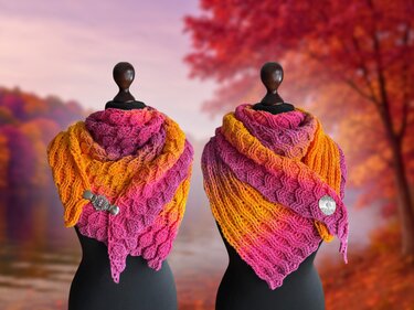 Zwei gehäkelte Dreieckstücher in Gelb, Orange und Pink mit Broschen auf Schaufensterpuppen vor herbstlicher Kulisse.