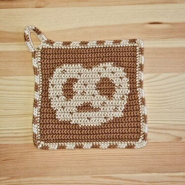 Braun-beiger quadratischer gehäkelter Topflappen mit zentralem Gesichtsmotiv und Aufhängeöse