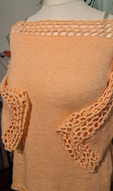 Apricotfarbener Sommerpullover mit Ajourmuster an Ausschnitt und Ärmeln, präsentiert auf einer Büste.