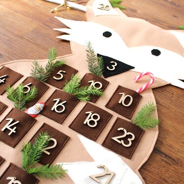 Beiger Filz-Adventskalender in Tierform mit braunen Filztaschen, nummerierten Holz-Zahlen und verschiedenen Füllungen