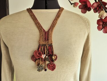 Boho-Halskette aus gehäkelten Blüten und Quasten in Braun- und Rottönen mit Perlen und Metallanhängern an hellem Pullover