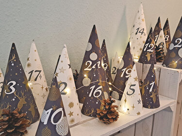 Selbstgemachter Adventskalender aus nummerierten Papierkegeln mit Lichterkette und Zapfen