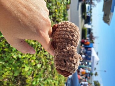 Nahaufnahme: Hand hält kleines braunes Amigurumi‑Tier als Größenvergleich