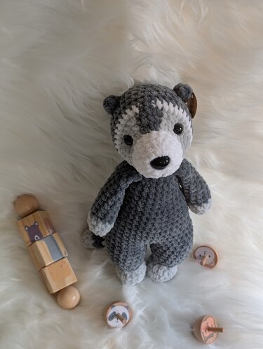 Gehäkeltes graues Amigurumi-Husky mit weißen Details auf hellem Fell, umgeben von Holzspielzeug