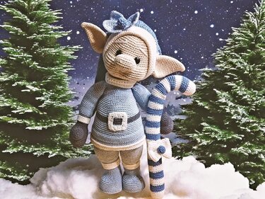 Handgehäkelter Wichtel in Blau- und Beige mit gestreifter Zuckerstange vor Schnee und Tannenbäumen