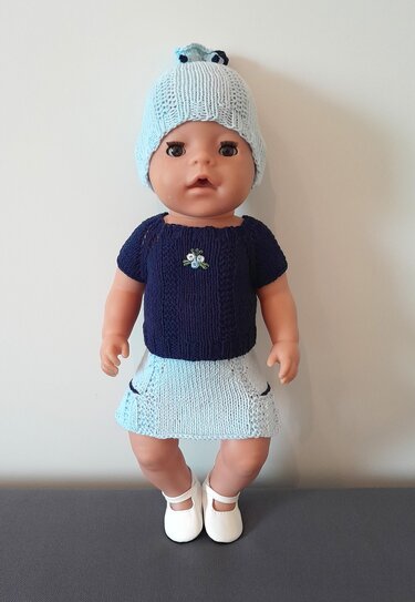 Puppe mit gestricktem dunkelblauen Kurzarm-Pullover, hellblauem Rock und Mütze