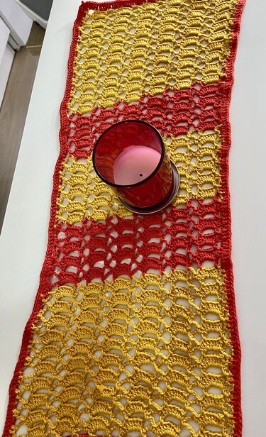 Gehäkelter Tischläufer in Rot und Gelb mit Muschelmuster und rotem Glas mit Kerze