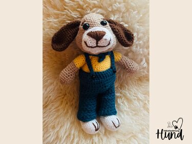 Gehäkelter Amigurumi-Hund mit gelbem Hemd und blauer Latzhose, liegend