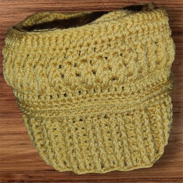 Senfgelbe gehäkelte Mütze mit ausgeprägtem Strukturmuster und geripptem Bund auf Holz