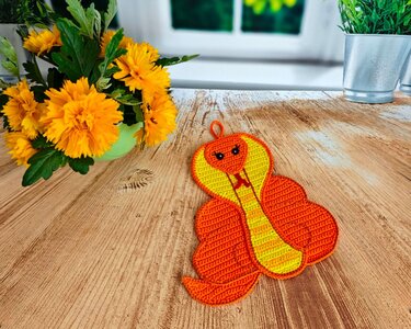 Orange and yellow crocheted cobra potholder with hanging loop on wooden table