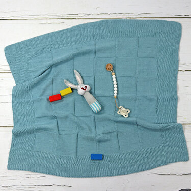 Hellblaue gestrickte Babydecke mit Stoffhase, Holzbausteinen und Schnullerclip