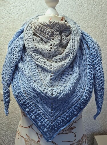 Gehäkeltes Dreieckstuch in Blau und Grau mit Farbverlauf und verschiedenen Häkelstichen auf einer Schneiderpuppe drapiert.