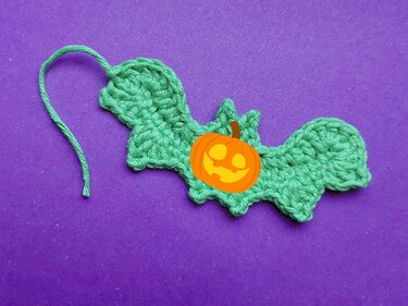 Grüne gehäkelte Fledermaus-Applikation mit Faden auf violettem Hintergrund
