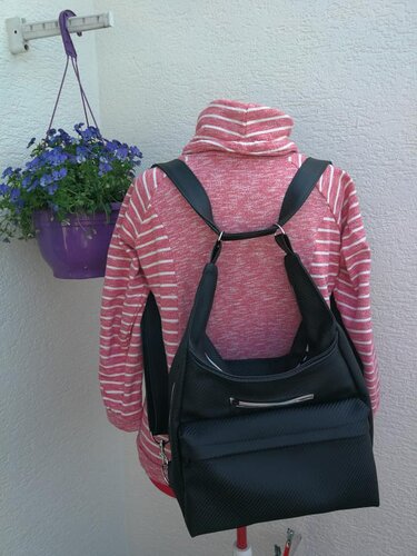 Schwarze wandelbare Tasche mit Reißverschluss, als Rucksack auf einer Schneiderpuppe mit rosa-weiß gestreiftem Oberteil.